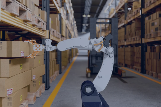 Bras robotique industriel saisissant un carton sur une étagère dans un entrepôt logistique, au milieu d’allées de stockage remplies de colis.